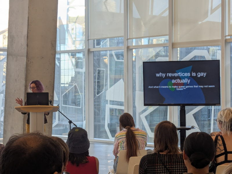 A speaker at a podium presents a slide to a seated audience at DEI or DIE v2: DEI Harder