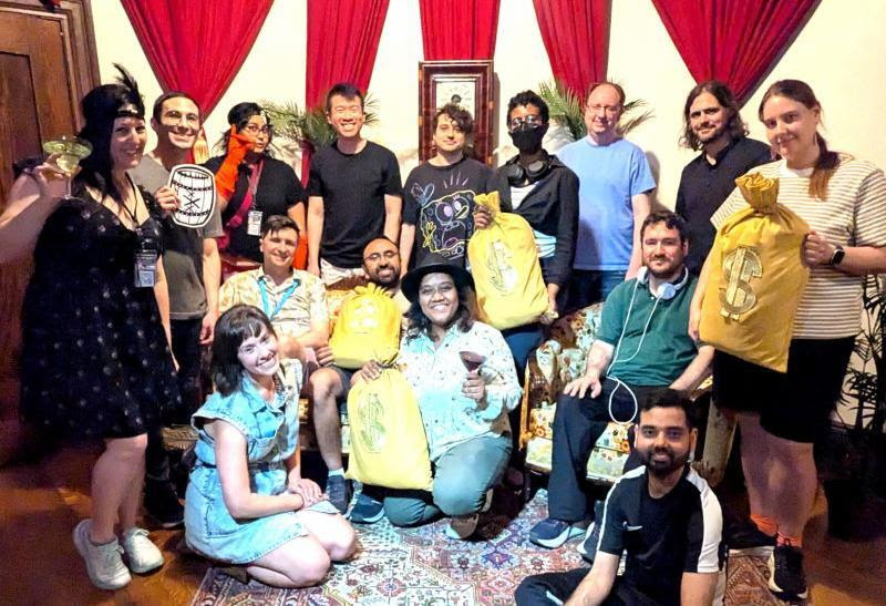 A group poses in front of red curtains holding money bag props