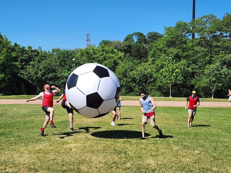 Players chase a giant inflatable soccer ball across a sunny field