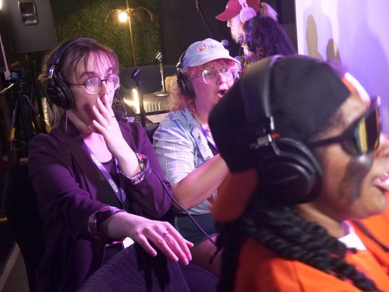 Three commentators wearing headphones react during a speedrunning broadcast
